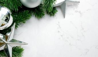 foglie di pino verde su sfondo di marmo bianco, decorazioni natalizie in colore argento brillante. concetto di natale semplice e creativo. foto