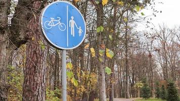 Segnale stradale pedonale e ciclabile con segni blu bianchi su uno sfondo di alberi e cielo blu in un parco in autunno. corsie separate per pedoni e ciclisti foto