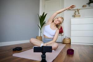 ritratto di giovane blogger, yoga soddisfare Creatore, mostrando esercizi, registrazione di se stessa Lavorando su a casa su gomma da cancellare stuoia foto