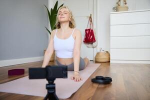 ritratto di giovane blogger, yoga soddisfare Creatore, mostrando esercizi, registrazione di se stessa Lavorando su a casa su gomma da cancellare stuoia foto