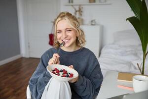 ritratto di giovane vlogger, soddisfare Creatore, mostrando sua fatti in casa prima colazione su telecamera, mangiare dolce, sorridente e guardare contento foto