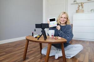 ritratto di bellissimo sorridente donna, registrazione nel sua camera, ha telecamera su caffè tavolo, rivedere trucco, fare stile di vita video blog per sociale media account, record un' lezione foto