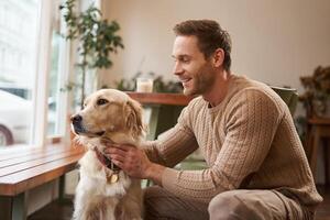 ritratto di giovane bello proprietario di un cane, la spesa tempo con il suo animale domestico nel un' bar, seduta al chiuso, guardare al di fuori finestra foto