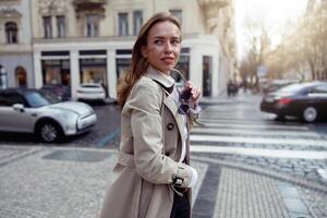 attraente donna nel cappotto attraversamento il città strada e guardare a lato. sfocato sfondo foto