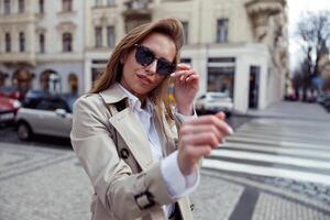 contento alla moda donna nel occhiali da sole in piedi su città strada sfondo e guardare a telecamera foto