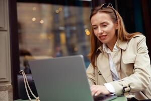 attraente europeo donna Lavorando su il computer portatile in linea mentre seduta a all'aperto bar terrazza foto