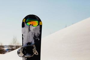 snowboard e occhiali da sci adagiati sulla neve vicino alla pista da freeride foto