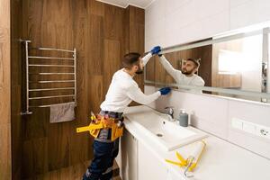 il lavoratore installa il specchio nel il bagno. foto