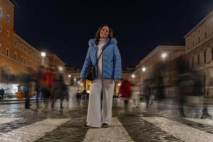 femmina turista in posa tra sfocato persone a piedi a notte su un' strada nel davanti di il Vaticano nel Roma foto