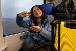 bella di mezza età donna in viaggio su il treno seduta tra il bagaglio Il prossimo per il finestra utilizzando il inteligente Telefono foto