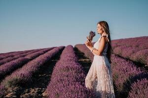 donna lavanda campo. contento spensierato donna nel un' bianca vestito a piedi nel un' lavanda campo e odorare un' lavanda mazzo su tramonto. ideale per caldo e ispirazione concetti nel voglia di girovagare e viaggio. foto