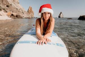 donna mare sup. vicino su ritratto di contento giovane caucasico donna con lungo capelli nel Santa cappello guardare a telecamera e sorridente. carino donna ritratto nel un' bianca bikini in posa su cenare tavola nel il mare foto