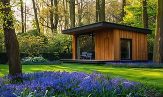 un' sereno moderno di legno cabina circondato di un' lussureggiante tappeto di campanule e non ti scordar di me nel un' tranquillo, calmo primavera giardino foto