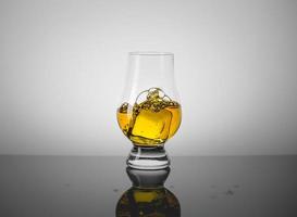 bicchiere da degustazione con un bicchierino di whisky scozzese e un cubetto di ghiaccio che cade dentro. foto