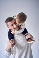 un' padre trasporta il suo figlio nel il suo braccia e giochi con lui nel un' minimalista studio foto