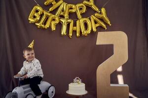 un' bambino piccolo è contento con un' compleanno torta e regali su il suo secondo compleanno foto