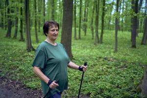 anziano donna è impegnato nel nordico a piedi con bastoni nel il primavera foresta foto