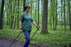 anziano donna è impegnato nel nordico a piedi con bastoni nel il primavera foresta foto