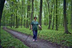 anziano donna è impegnato nel nordico a piedi con bastoni nel il primavera foresta foto