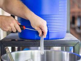 avvicinamento di dell'uomo mano Tenere un' Cacciavite per serrare il gomma da cancellare cinghia per permettere il mestiere birra flusso fuori. selettivo messa a fuoco. birra fatta in casa processi foto