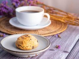 avvicinamento di un' biscotto su un' piatto con un' bianca caffè tazza e fiore sfocato sfondo. spazio per testo foto