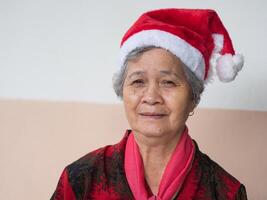 anziano donna indossare un' Santa Claus cappello e guardare a il telecamera. concetto di anziano persone e Natale e nuovo anno Festival foto