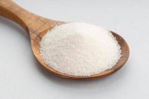 zucchero in cucchiaio di legno su sfondo grigio foto