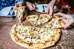 persona taglio un' fetta di Pizza su un' tavolo foto