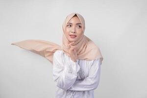 elegante giovane asiatico musulmano donna indossare bianca vestito con hijab agitando nel il vento, modellazione posa su bianca sfondo foto