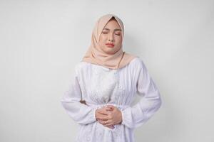 giovane asiatico musulmano donna nel bianca vestito e crema velo hijab Tenere sua stomaco sensazione Affamato durante digiuno. Ramadan concetto foto