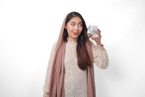 sorridente asiatico musulmano donna è Tenere un' bicchiere di acqua nel digiuno mese al di sopra di isolato bianca sfondo. Ramadan e eid mubarak concetto foto