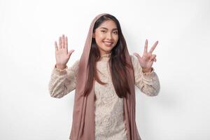 ritratto di attraente asiatico musulmano donna indossare velo hijab dando numero uno per dieci di mano gesto, in piedi al di sopra di isolato bianca sfondo foto