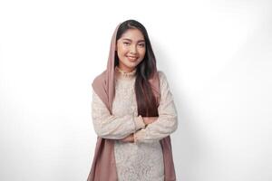 giovane asiatico musulmano donna indossare foulard velo sorridente per il telecamera con attraversato braccia posa pieno di fiducia, isolato di bianca sfondo foto