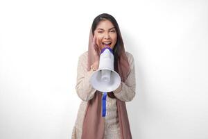 vivace giovane asiatico musulmano donna indossare foulard velo hijab urlando a megafono, isolato su bianca sfondo studio. Ramadan e eid mubarak concetto. foto