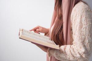 vicino su ritratto di asiatico musulmano donna nel foulard velo hijab Tenere e lettura al Corano al di sopra di isolato bianca sfondo. Ramadan e eid mubarak concetto. foto