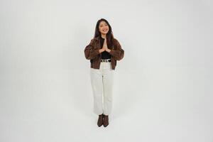 un' pieno corpo ritratto di asiatico giovane donna con casuale attrezzatura fabbricazione saluto gesto con Due mani mentre sorridente, in piedi su isolato bianca sfondo foto