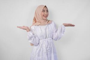contento asiatico donna indossare hijab e bianca vestito puntamento su e presentazione il opzione su copia spazio sopra, in piedi al di sopra di isolato bianca sfondo. Ramadan e eid mubarak annuncio pubblicitario concetto foto