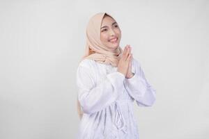 bellissimo asiatico musulmano donna indossare bianca vestito e hijab sorridente mentre fare formale benvenuto o saluto gesto, in piedi al di sopra di isolato bianca sfondo foto