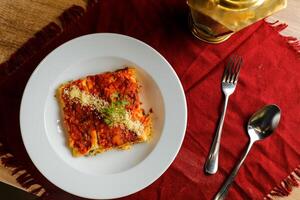 speziato pomodoro e Manzo Lasagna servito nel piatto con forchetta e cucchiaio isolato su rosso tovagliolo superiore Visualizza di veloce cibo su tavolo foto