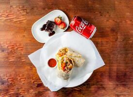 pollo avvolgere pieno con cetriolo, cipolla e pomodoro con peperoncino salsa, folletto buono e Coca Cola può 330 ml servito nel piatto isolato su di legno tavolo superiore Visualizza di hong kong cibo foto