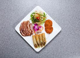 tailandese aperitivo piatto con grigliato Maiale collo fetta, siamese pesce torta, tailandese primavera rotolo e senza ossa pollo piedi insalata servito nel piatto isolato su grigio sfondo superiore Visualizza di hong kong cibo foto