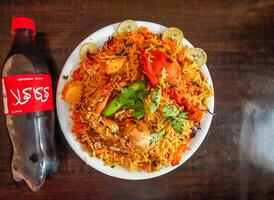 speziato pollo biryani con Patata metà rifiuti Coca Cola bottiglia 500 ml, cipolla e Limone fetta servito nel piatto isolato di legno sfondo superiore Visualizza indiano spezie e pakistano cibo foto