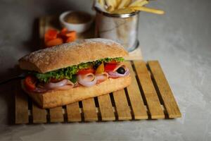 Ciabatta affumicato prosciutto Sandwich isolato su di legno con Maionese tuffo e francese patatine fritte secchio tavola lato Visualizza di italiano veloce cibo su grigio sfondo foto