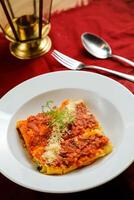 speziato pomodoro e Manzo Lasagna servito nel piatto con forchetta e cucchiaio isolato su rosso tovagliolo lato Visualizza di veloce cibo su tavolo foto