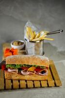 Ciabatta affumicato prosciutto Sandwich isolato su di legno con Maionese tuffo e francese patatine fritte secchio tavola lato Visualizza di italiano veloce cibo su grigio sfondo foto