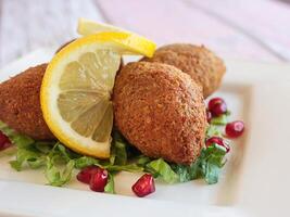 kebbah, kibbeh, kibbe o kubbeh con Limone fetta e Melograno semi avvicinamento servito nel piatto isolato su tavolo lato Visualizza di Arabo Fast food foto