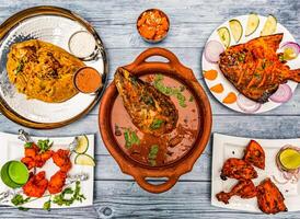 pesce testa curry, darbar reale potlam biryani Riso, tandoori pollo, griglia pomfret pesce, rava kesari halwa dolce, pollo lecca-lecca, servito nel piatto isolato di legno tavolo superiore Visualizza di indiano speziato cibo foto