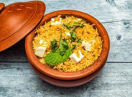 paneer biryani riso servito nel vaso di terracotta piatto isolato su di legno tavolo superiore Visualizza di indiano speziato cibo foto