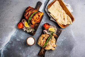 metà grigliato pollo piatto griglia con Pita pane, nonna, tandoori Roti, rata, tuffo e insalata, pomodoro cipolla e Limone servito nel di legno tavola superiore Visualizza su sfondo speziato barbeque foto