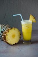 salutare ananas fresco succo servito nel bicchiere con ananas fetta e cannuccia lato Visualizza su grigio sfondo foto